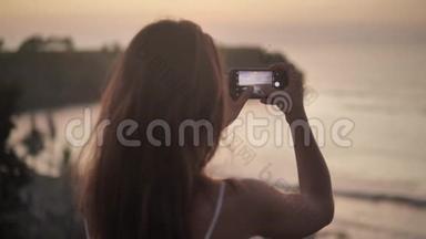 年轻的女人手拿智能手机，做自然摄影。 年轻旅游女用手机拍照